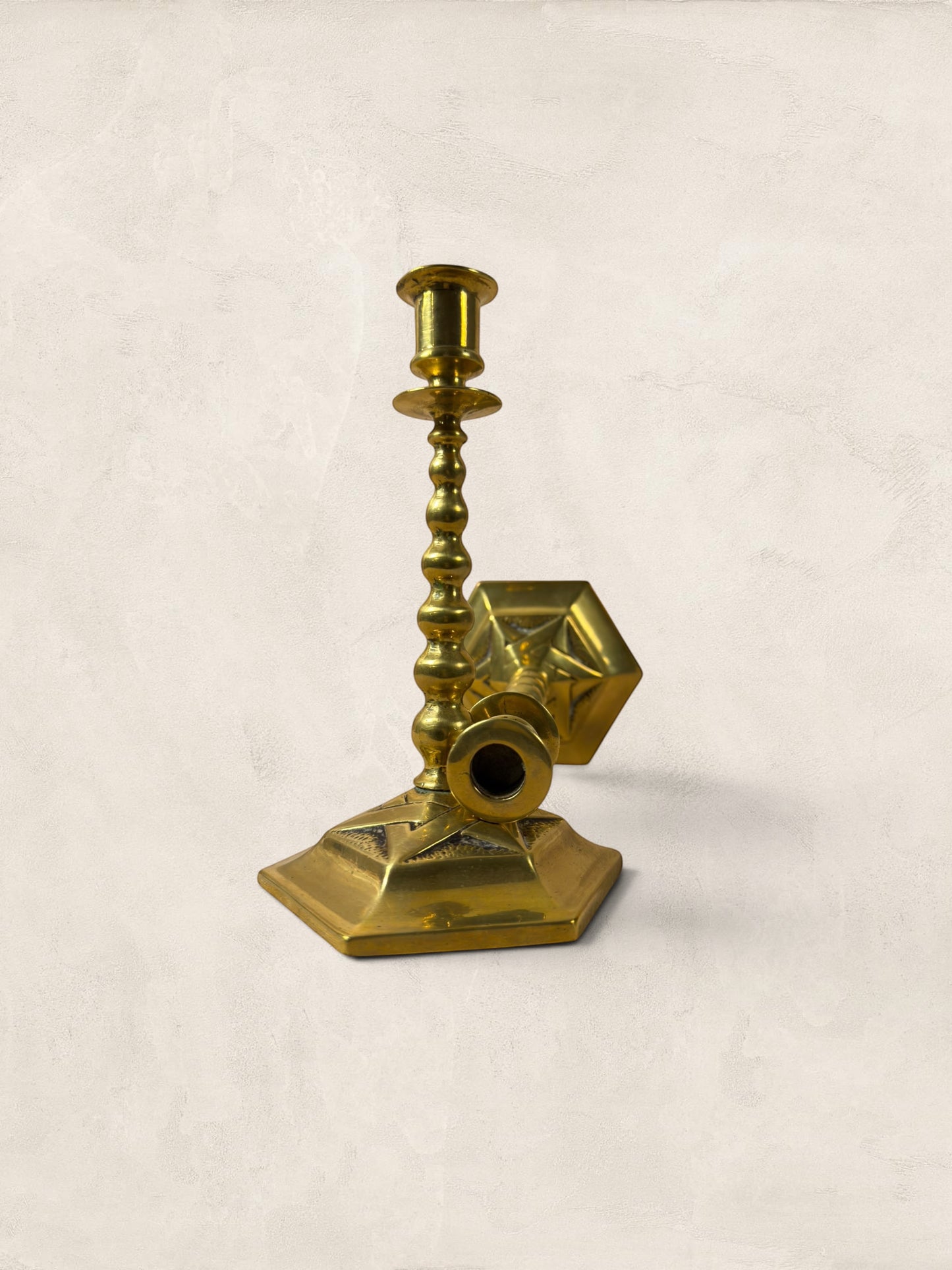 Stone and Relic pair of vintage 1920s brass candlesticks with weighted square bases and ornate stems, showing aged patina.